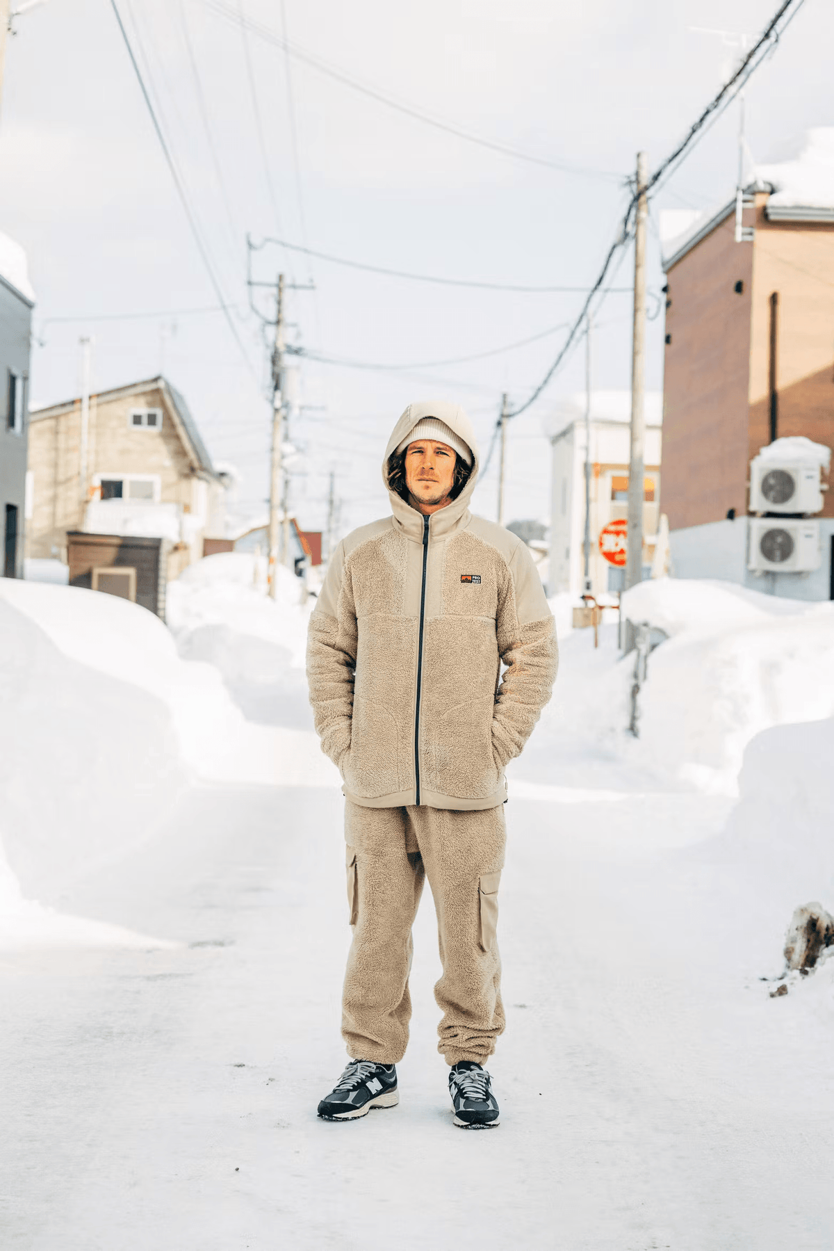 Homme en sweat beige à capuche et zip dans un paysage enneigé